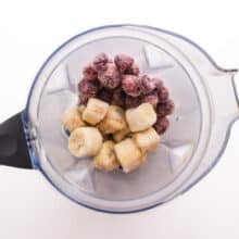 frozen cherries and bananas are in the bottom of a blender jar.