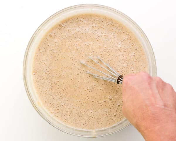 A hand holds a whisk stirring cake batter in a bowl.