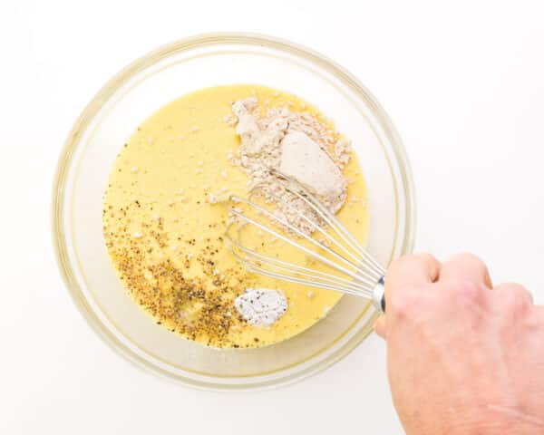 A hand whisks faux egg mixture with several ingredients in a bowl.