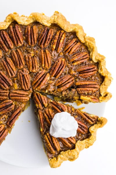 Looking down on a vegan pecan pie with a slice cut out. The slice has whipped cream on top.