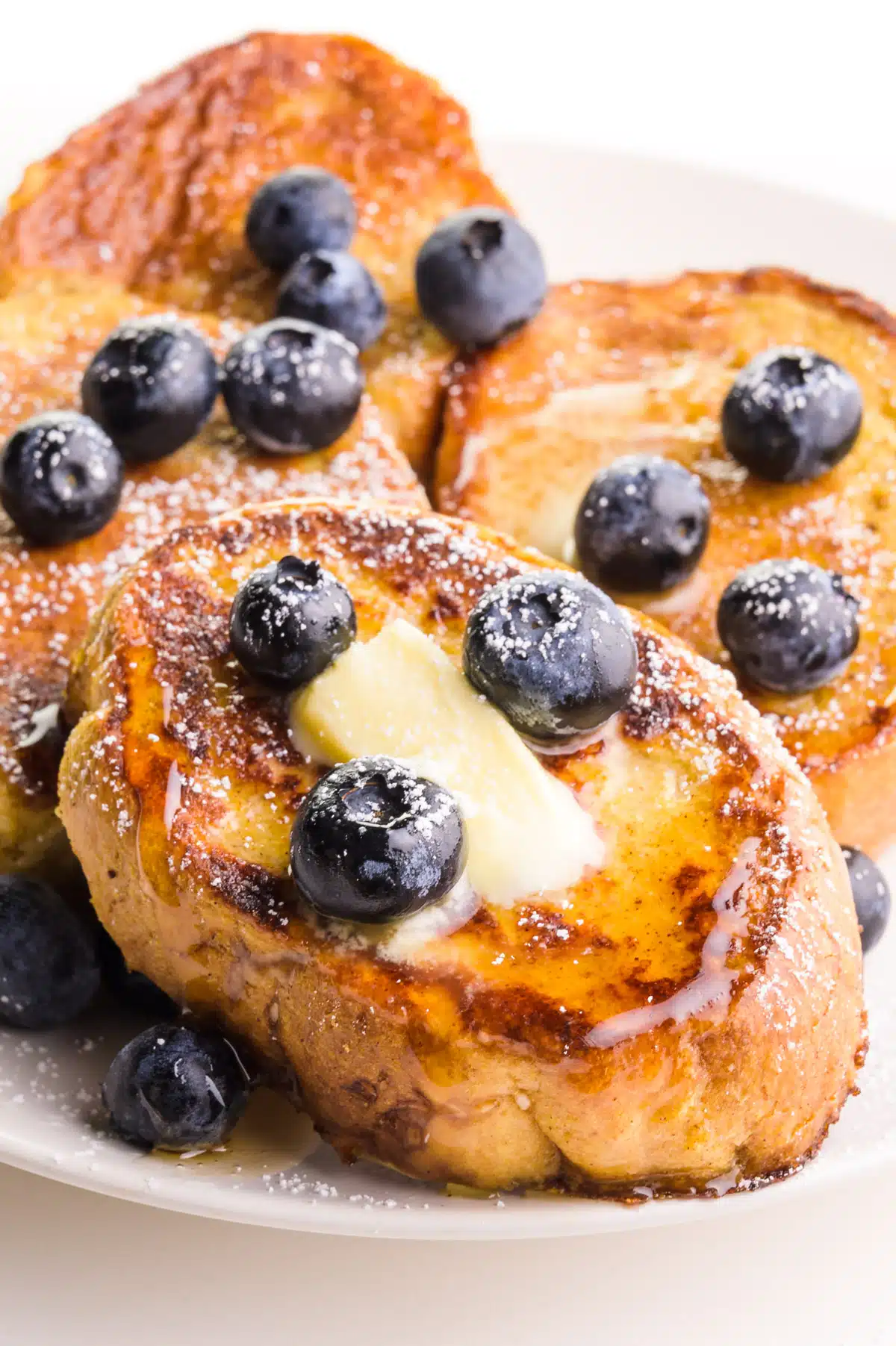 Slices of French toast are topped with blueberries, butter, and maple syrup.
