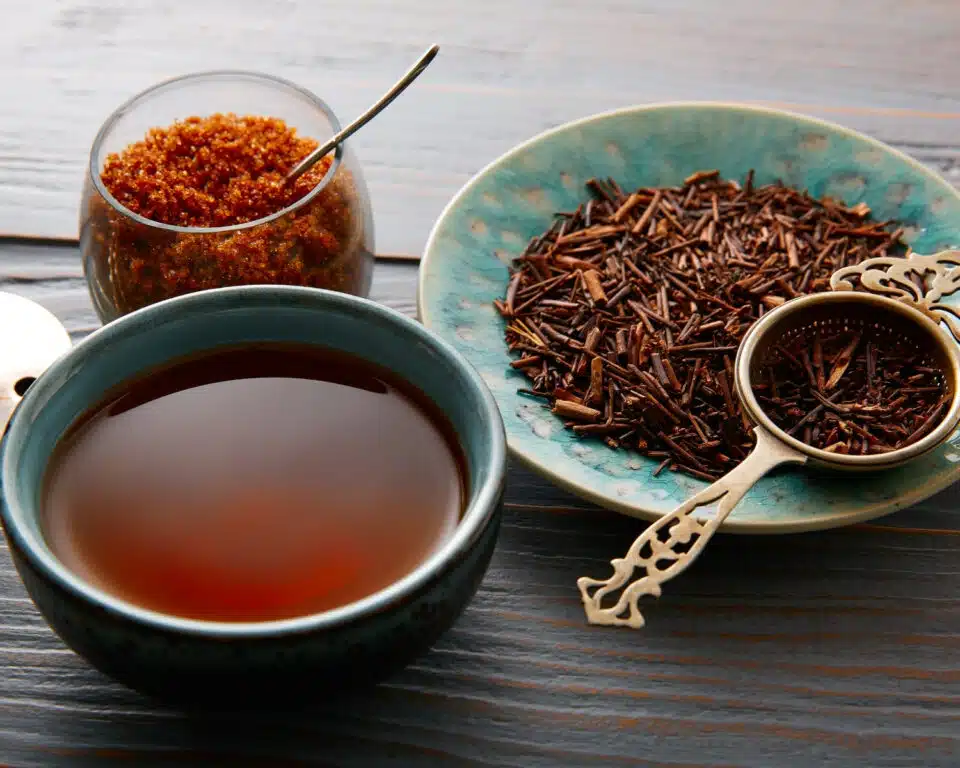 A bowl of tea sits in front of a plate with kukicha twigs with a tea dipper and a glass bowl with a spoon in it.