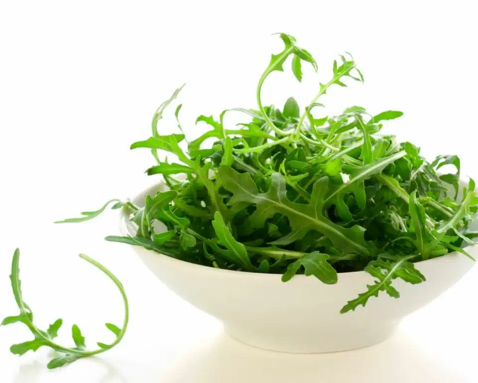 A photo of rocket greens in a bowl. One of the greens is sitting next to the bowl.