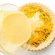 A vegan egg mixture is being poured over a pie crust with cheese and other ingredients.