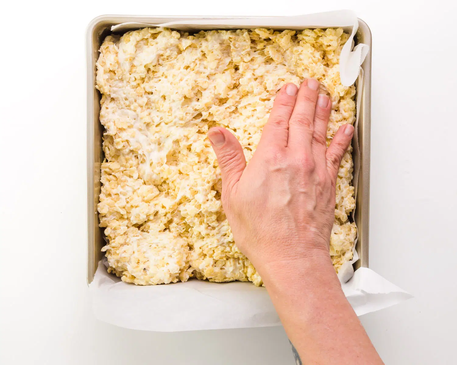 A hand presses dairy-free Rice Krispie treats into a pan.